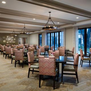 A spacious dining room with neatly arranged tables and chairs, illuminated by elegant lighting fixtures.