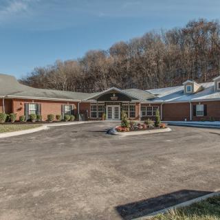 A brick residential building with a parking lot surrounded by trees.