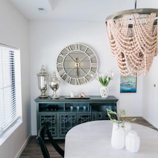 A stylishly decorated dining area featuring a large wall clock, an elegant chandelier, and a sideboard with decorative items.