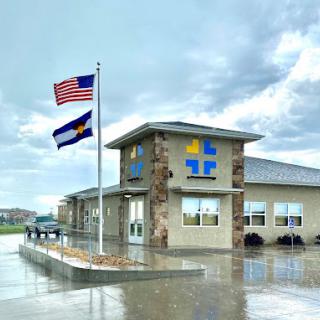 A modern public building with the American and Colorado flags displayed under a cloudy sky.