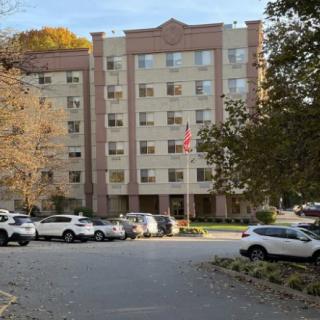 A residential apartment building with a parking lot full of cars and surrounded by trees.