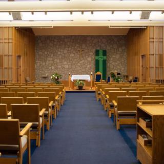 A peaceful chapel interior with rows of seating, an altar, and a prominent cross at the front.