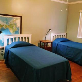 A bedroom with two twin beds featuring blue bedding, a nightstand with a lamp between them, and a large map on the wall.