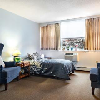 A cozy bedroom featuring a bed, chairs, and a window with curtains.