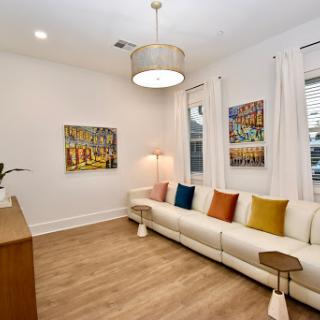 A bright and modern living room featuring a stylish white sofa adorned with colorful cushions, complemented by warm wooden elements and vibrant artwork.