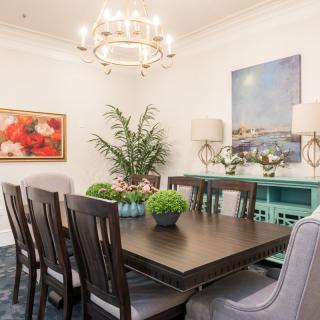 A beautifully decorated dining room with a centerpiece chandelier, art on the walls, and indoor plants adorning the space.