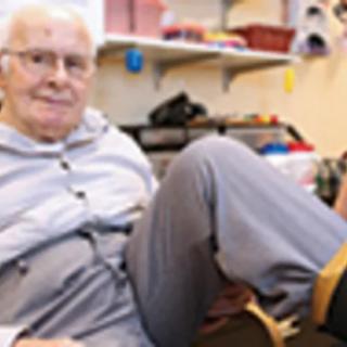An elderly person sitting comfortably in a room, wearing casual clothing.