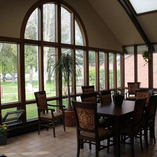A sunlit dining area with large windows and wooden furniture.