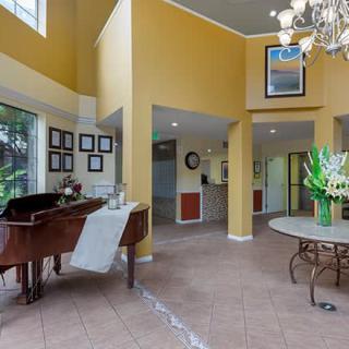 A spacious living room with a grand piano, elegant chandelier, and large windows allowing natural light.