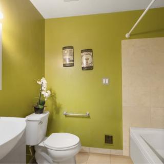 A modern bathroom with green walls and minimalist decor, featuring a toilet, sink, and bathtub.