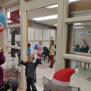 Children playing with balloons indoors near a large window.