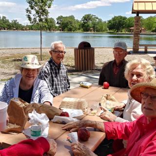 A group of elderly people enjoying a picnic by the lake in a park.
