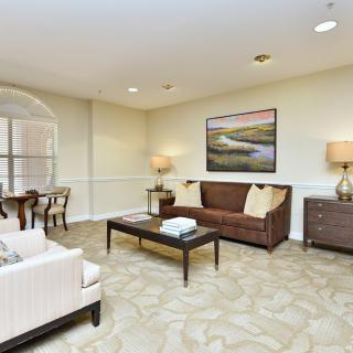 A cozy living room with a comfortable sofa, coffee table, and stylish artwork on the wall. The room features elegant lighting and an adjoining dining area.