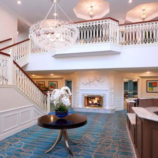 A modern hotel lobby featuring a grand chandelier, a cozy fireplace, and an elegant staircase.
