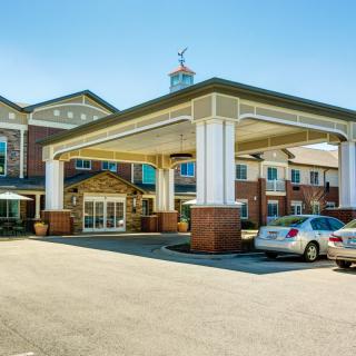 A view of a building with a covered entrance and parked cars in the driveway.