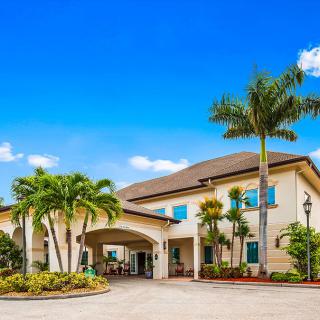 A tropical-style building with palm trees and a landscaped entrance on a sunny day.