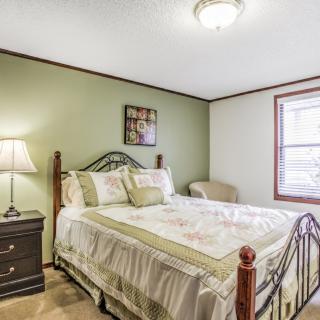 A cozy bedroom with a double bed, green accent wall, and natural light coming through the window.