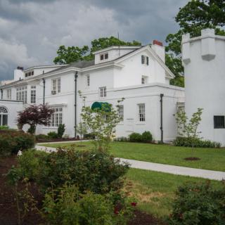 A large white house with a well-maintained garden and a cloudy sky in the background.