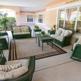 A cozy patio area featuring green wicker furniture with cushions, a central rug, and surrounding plants.