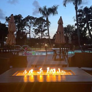 A cozy evening view by the fire pit near a pool, surrounded by palm trees.