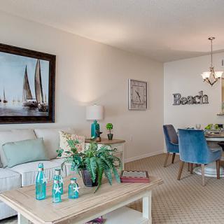 A cozy living and dining space with a coastal theme, featuring blue chairs, sailboat artwork, and beach-inspired decorations.
