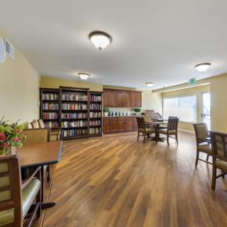 A cozy library with bookshelves, tables, and chairs, featuring a warm wooden floor and soft lighting.