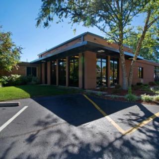 A modern office building with a parking lot surrounded by trees on a sunny day.