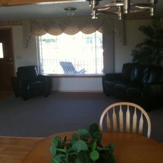 A cozy living room with two chairs, a large window, and a dining table with an indoor plant.