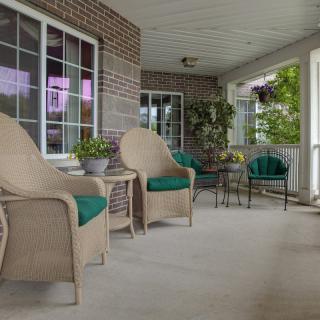 A cozy porch with comfortable chairs and a table, decorated with plants and greenery.