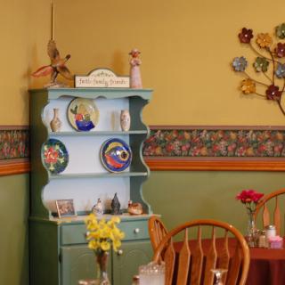 A cozy vintage kitchen corner with a light blue cabinet, decorated with colorful plates and surrounded by floral wallpaper.