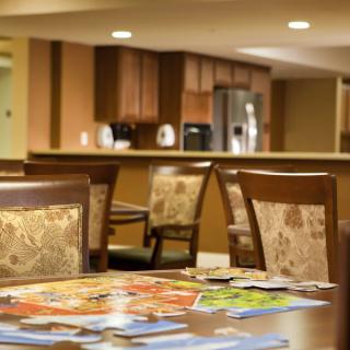 A cozy dining area with a wooden table and chairs, featuring magazines on the surface and a kitchen in the background.