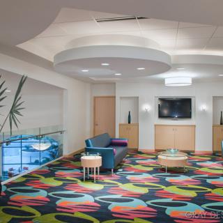 A modern lobby featuring colorful carpets, minimalist furniture, and a wall-mounted television.