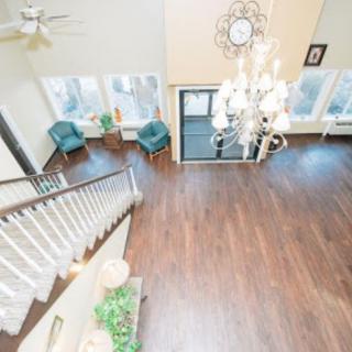 A spacious living room with hardwood flooring, a grand chandelier, and ample natural light.