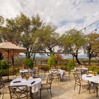 A serene patio setup with tables and chairs, surrounded by trees and overlooking a scenic view.