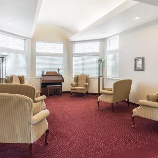 A cozy living room with a piano, surrounded by comfortable chairs and large windows.