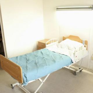 An empty hospital bed with a blue blanket in a bright room.