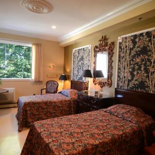 A cozy hotel room featuring twin beds with patterned bedspreads, elegant lamps, and a decorative mirror.