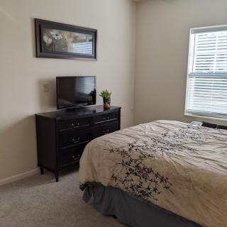 A cozy bedroom with a bed, dresser, and television near a window.