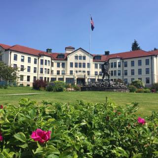 A historic building with red roofs surrounded by a lush garden and vibrant flowers under a clear blue sky.