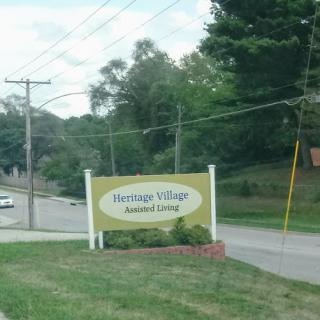 Entrance sign for Heritage Village Assisted Living, set in a green landscape.
