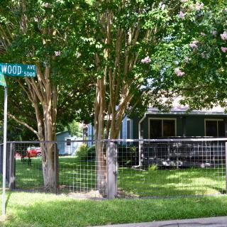 A suburban street corner with trees and a fenced yard.