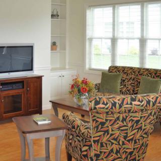 A cozy living room with patterned sofas, a television on a stand, and a large window providing natural light.