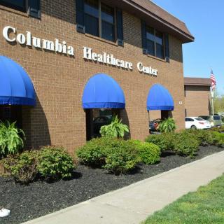 A brick healthcare center with blue awnings and landscaped surroundings.