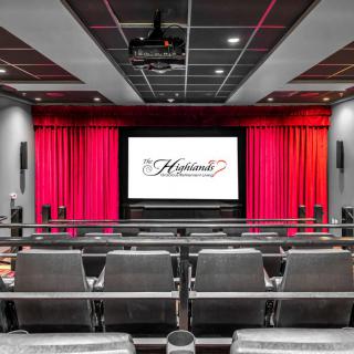 A luxurious home theater setup with comfortable seating and a large screen, framed by red curtains.