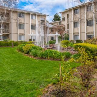 A residential apartment complex featuring a well-maintained lawn and a central fountain.
