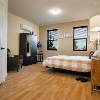 A cozy bedroom with a simple, minimalist design featuring a bed, wardrobe, and lamp.