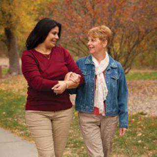 Two women walking arm in arm in a park during autumn.