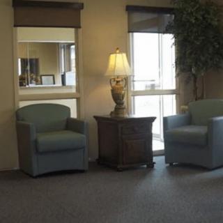 A cozy seating area with two armchairs flanking a side table topped with a lamp, next to a window and mirror.
