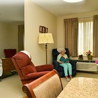 A senior person sits in a comfortable armchair in a cozy living room.