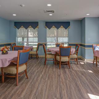 A well-lit dining area with neatly arranged tables and chairs, featuring large windows with blue curtains.